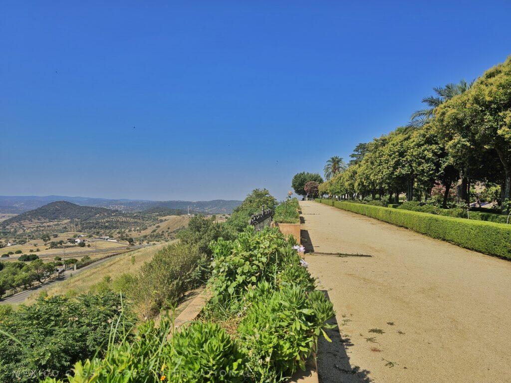 photo taken looking along the path in a park, trees on right, view over countryside on left. blue sky