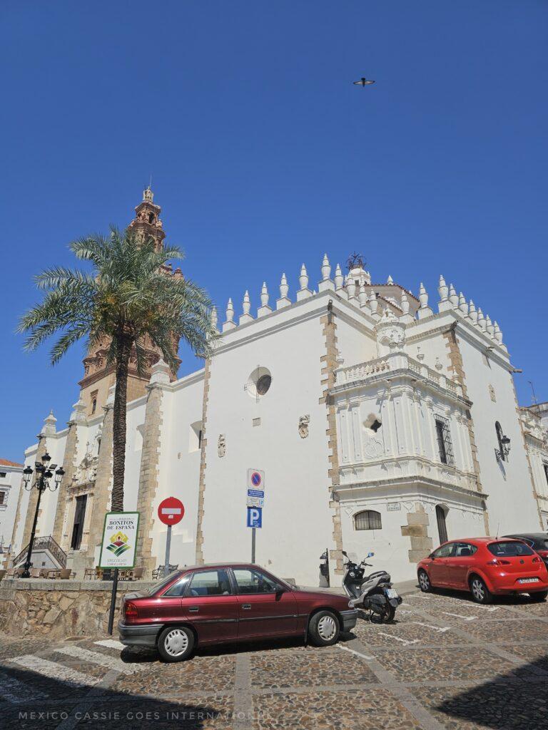 white church on a plaza, cars and a bike parked at base