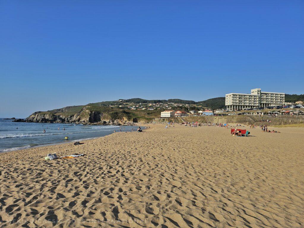 beach in galicia, people in distance by headland, white building on right