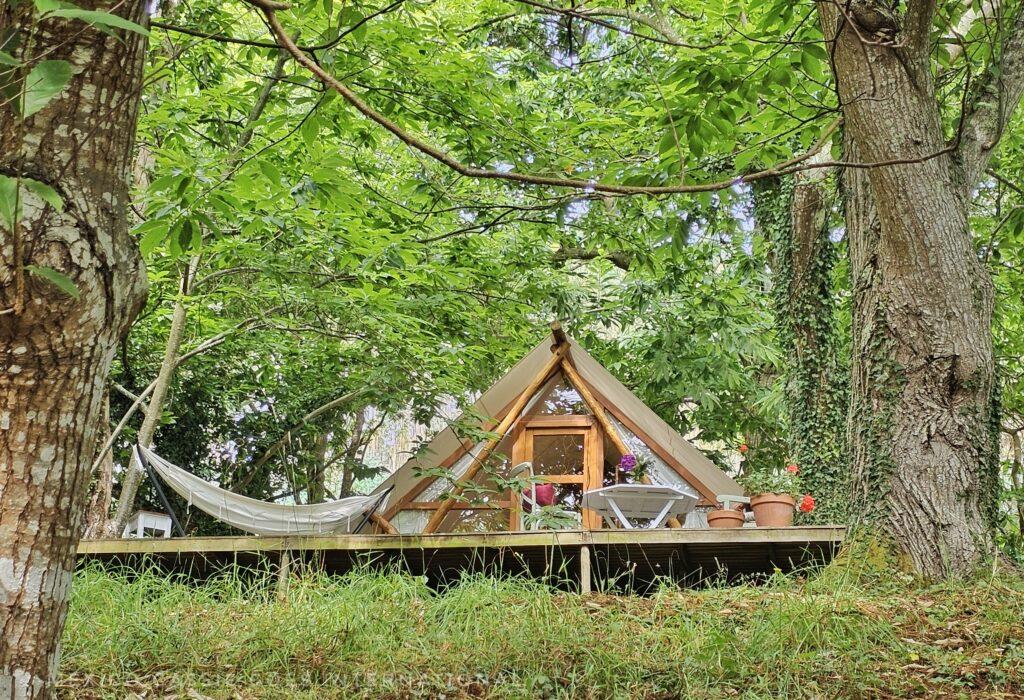 glamping tent under green trees, hammock on one side
