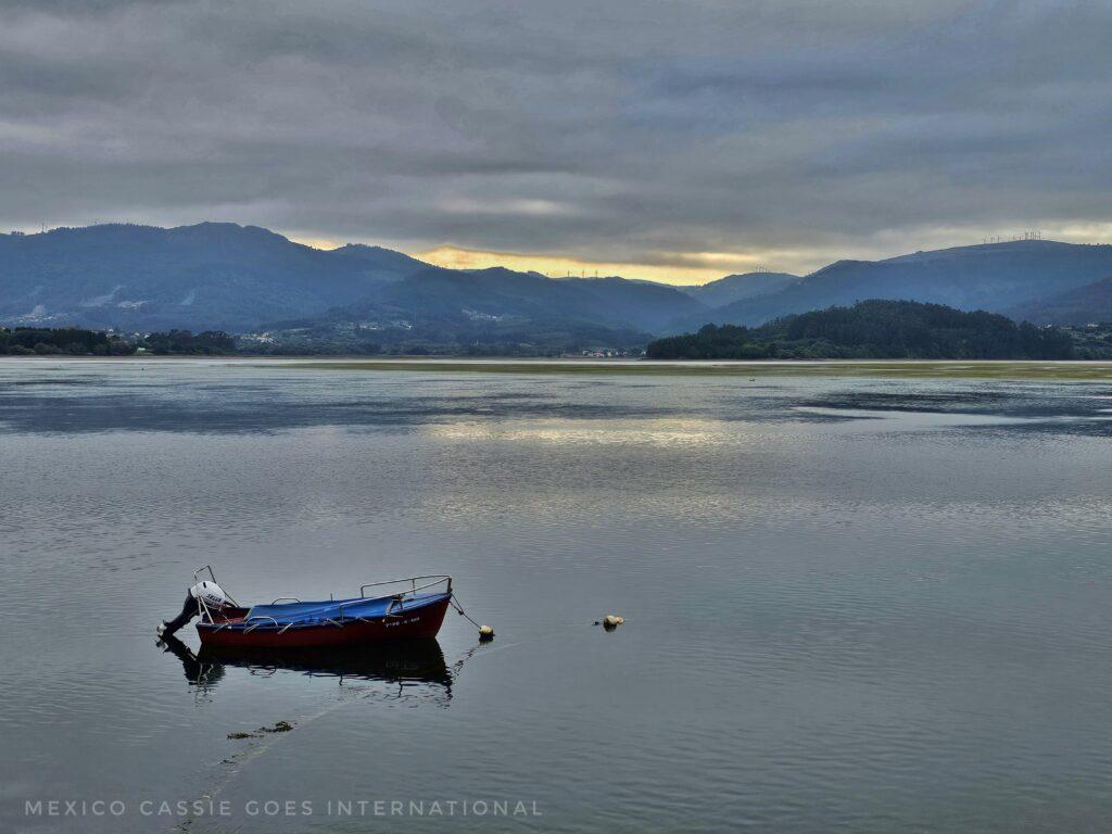 estuary at Ortigueira - solitary rowing boat moored in water, hills in background, last light of the day