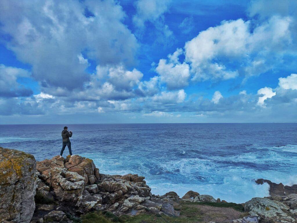 Cass standing on rocks taking a photo of the violent sea