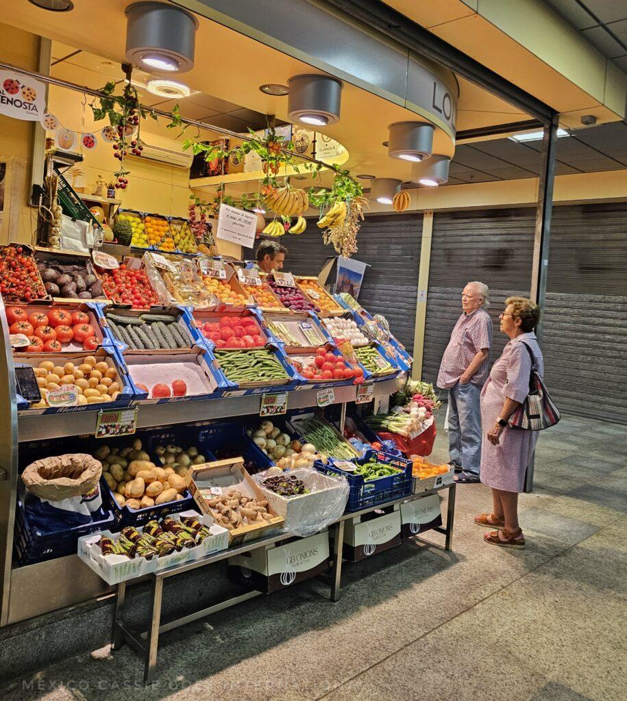fruit and veg market stall in Sevilla. two people standing near looking at the products