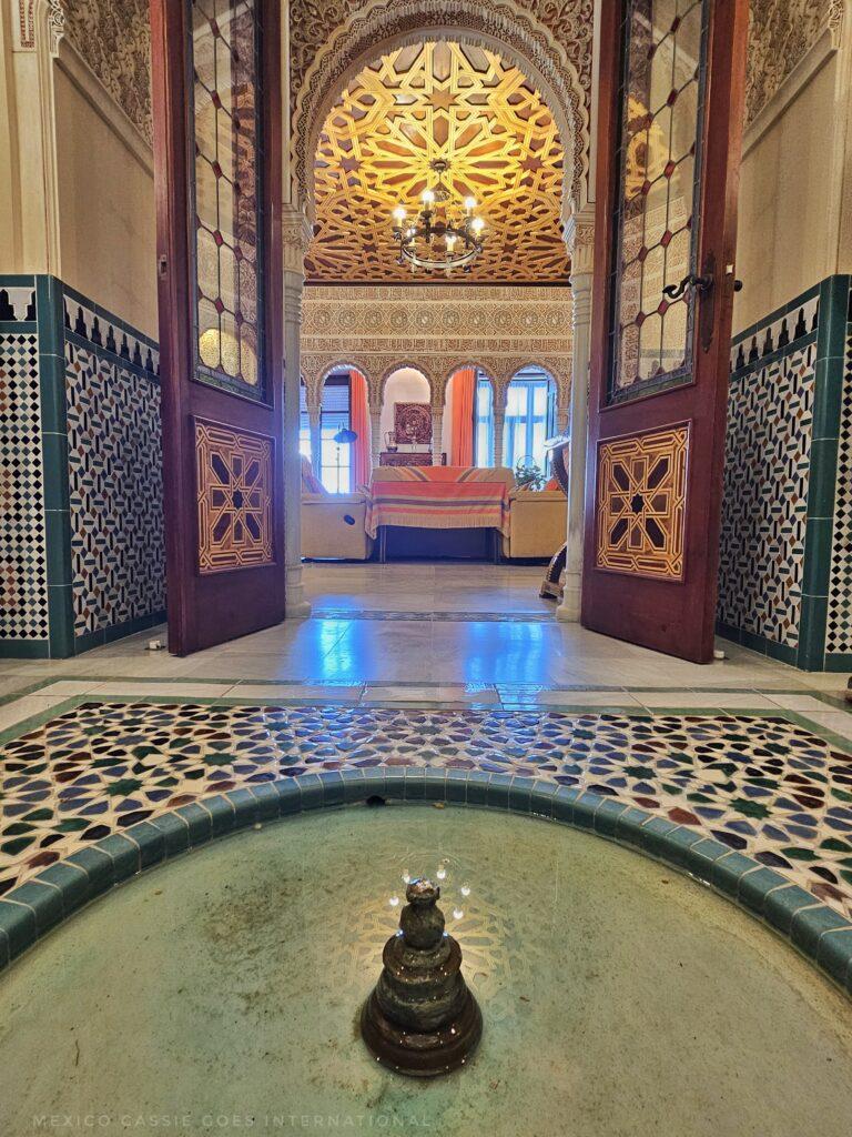 small fountain in floor in front of open doors, tiled walls, sofa in far end 