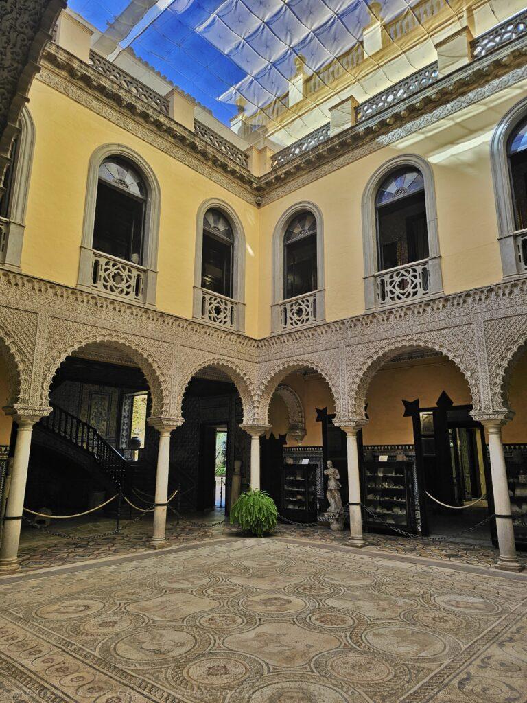 courtyard with mosaic floor, arches, yellow walls and windows on first floor