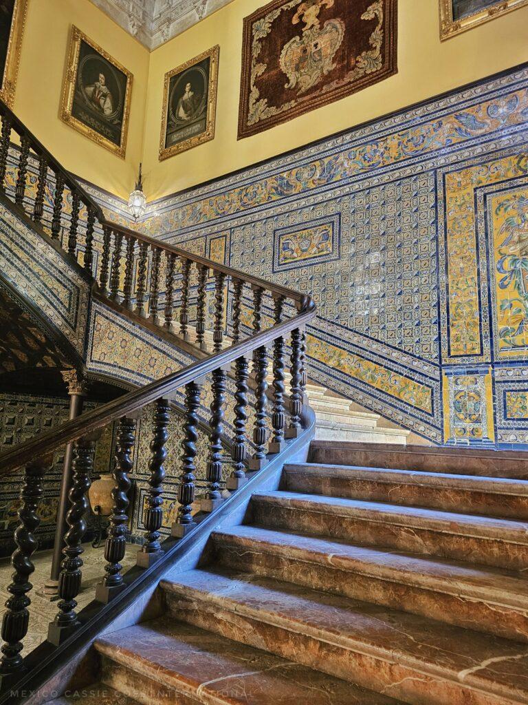 large fancy stair case with tiled walls and paintings above the tiles