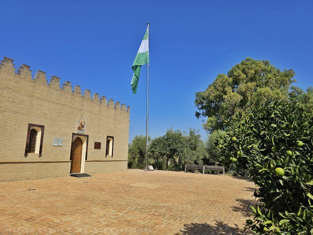 one storey brick building with green and white andalus flag flying. trees around