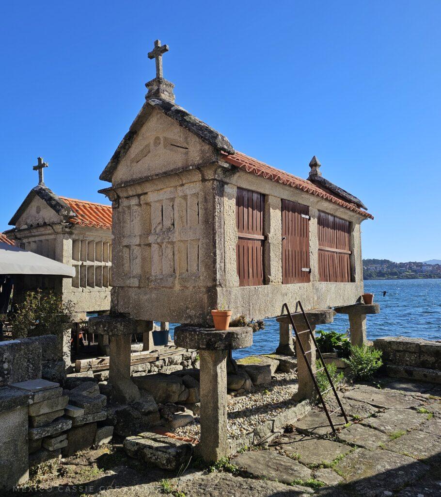 hórreo  with three wooden windows, tiled roof, cross on top and riased up off ground