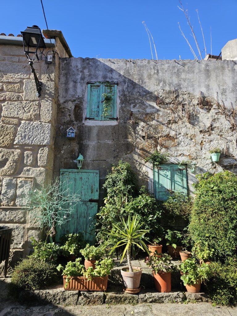 granite house with light green door and shutters, plants in pots