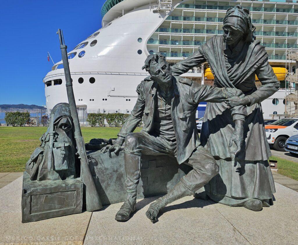 sculpture of a woman helping a soldier who is sitting down with his luggage - modern cruise ship behind them