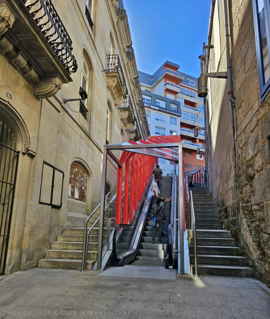 escalator between two buildings, stairs on either side, red 'wall' and bars over the top