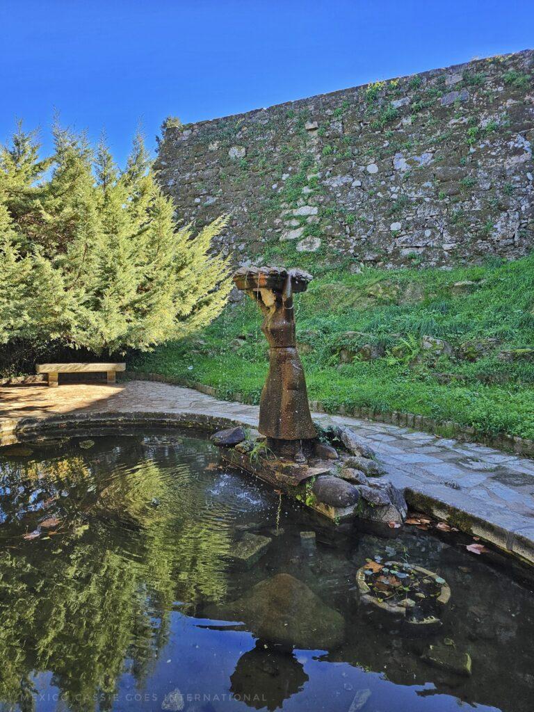 pond with sculpture of a woman, fortress wall and tree behind