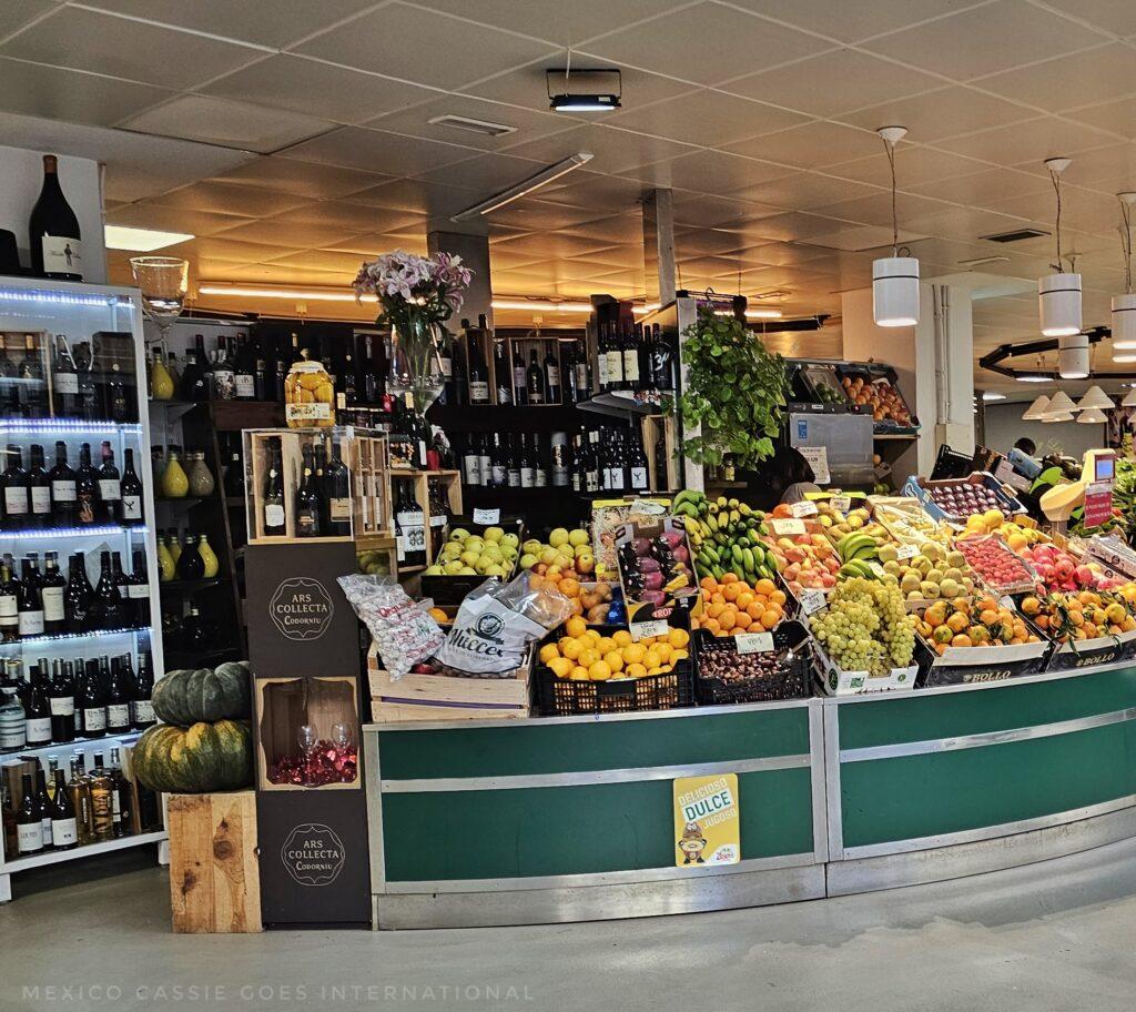 market stall full of fresh fruit, wine to side and behind