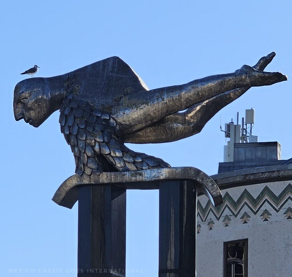 modern sculpture of a mermaid with a real pigeon perched on its head