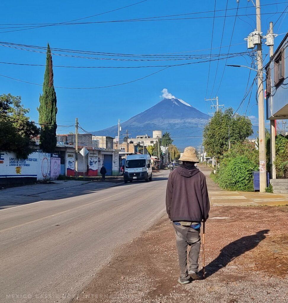 man walking by side of empty road, smoking volcano in front